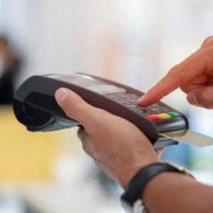 Cashier holding credit card reader machine on hand with insert card for payment process from customer, pressing the value number or price of products to charge the online payout, online deduction
