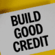 Calculator and magnifying glass on a yellow background with a sign that reads Build Good Credit.
