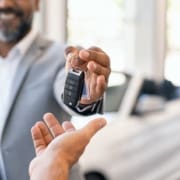 A car dealer handing over keys to a new car owner in a bright showroom.