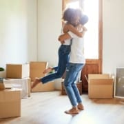 A couple celebrating in their new home surrounded by cardboard moving boxes.