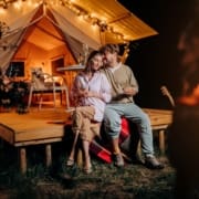 A couple enjoying a romantic evening with wine outside a luxury glamping tent at night.